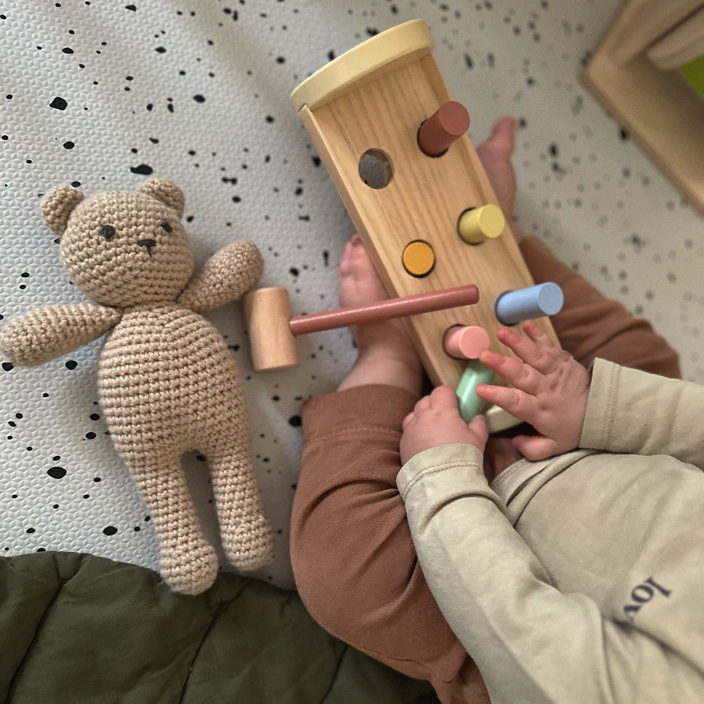 Child playing with a wooden hammer and block set on copenhagen kid play mat